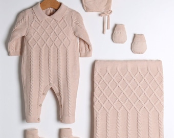 May include: A matching baby clothing set in a soft pink hue. The set includes a romper, bonnet, socks, booties, and a blanket. The romper and blanket feature a cable knit and diamond pattern.