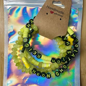 May include: Three neon green and black beaded bracelets spelling out "Neon Ghost" and "Radiation". The bracelets are presented in a holographic bag with a tag that reads "Handmade with love".