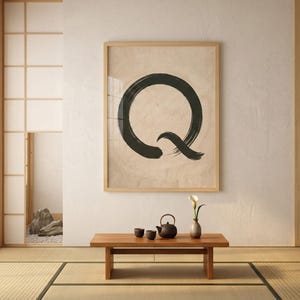 Könnte beinhalten: Ein gerahmtes Kunstwerk mit einem großen schwarzen Pinselstrich 'Q' auf beigem Hintergrund hängt über einem niedrigen Holztisch. Auf dem Tisch stehen eine Teekanne, Tassen und eine Vase mit einer weißen Blume. Der Raum hat eine japanische Ästhetik.