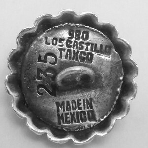 May include: A silver button with a scalloped edge. The button has the text "980 Los Castillo Tango 235 Made in Mexico" engraved on it.