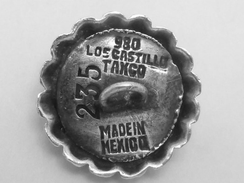 May include: A silver button with a scalloped edge. The button has the text "980 Los Castillo Tango 235 Made in Mexico" engraved on it.