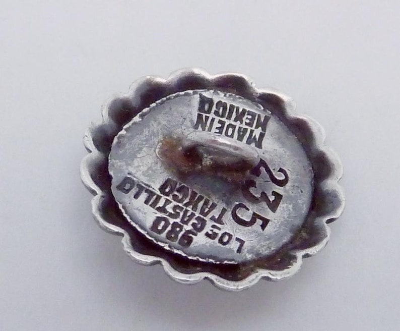 May include: Silver button with a scalloped edge. The button has the text "MADE IN MEXICO" and "LOS CASTILLO" with the number "23" and "980" printed on it.