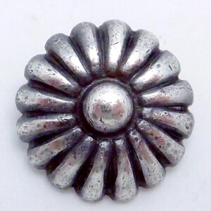 May include: A silver-toned metal button with a raised, circular center and a decorative, sunburst-like design around the edge.