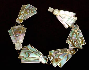 May include: A silver-toned bracelet featuring iridescent abalone shell segments in a fan-like design. The segments are outlined in silver and connected by small, round links. The bracelet is set against a black background.