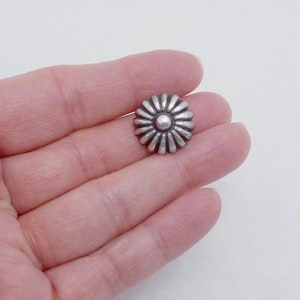 May include: Silver-toned metal flower-shaped button with a raised center. The button has a textured, daisy-like design.