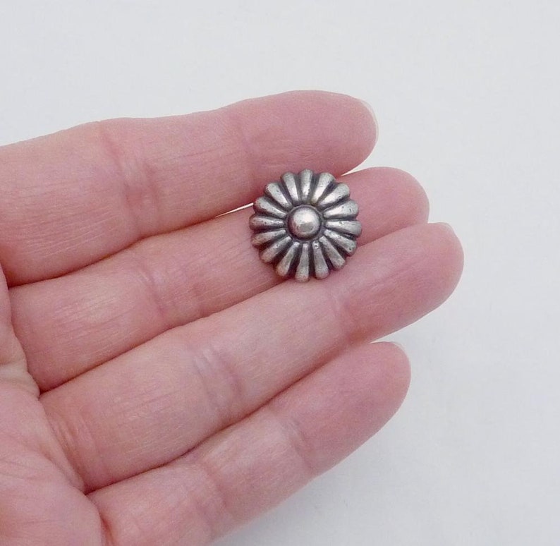 May include: Silver-toned metal flower-shaped button with a raised center. The button has a textured, daisy-like design.