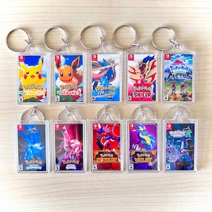 May include: Ten clear acrylic keyrings displaying Pokémon game covers, including "Pokémon Sword," "Pokémon Shield," and "Pokémon Scarlet." Each keyring features colourful illustrations of characters and game titles, perfect for fans of the franchise.
