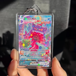 May include: A Gengar VMAX Pokemon card in a clear plastic holder. The card features a purple and red Gengar character with the text "Fear and Panic" and "G-Max Swallow Up". The card is a Single Strike card.