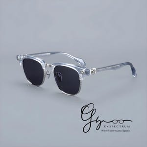 May include: Clear-framed sunglasses with dark lenses. The sunglasses have a silver metal bridge and decorative accents on the temples. The temples are embellished with small, clear stones. The image includes the text "G Spectrum" and "Where Vision Meets Elegance."