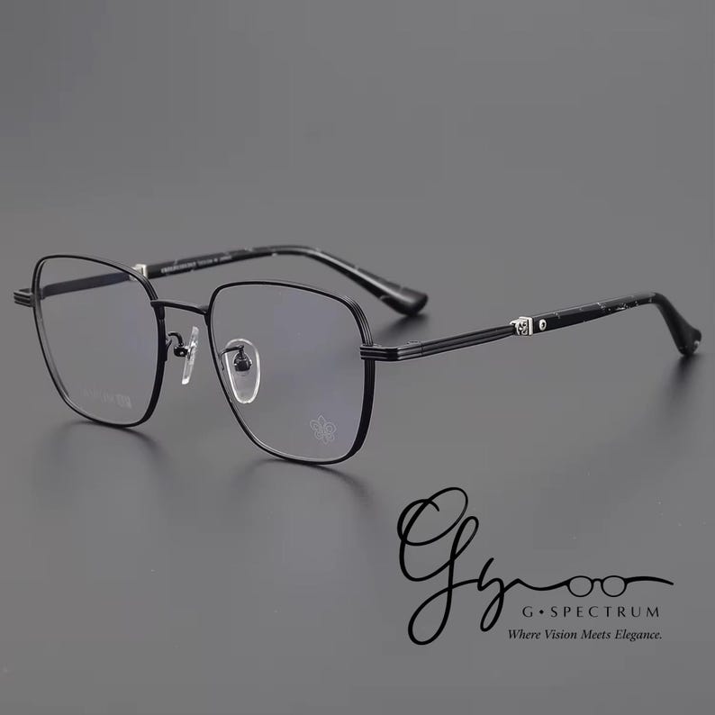 Puede incluir: Gafas con montura met&aacute;lica negra de forma cuadrada. Las gafas tienen un doble puente y un peque&ntilde;o emblema en la lente inferior derecha. Las patillas son finas y tienen un elemento decorativo. El texto "G Spectrum" es visible.