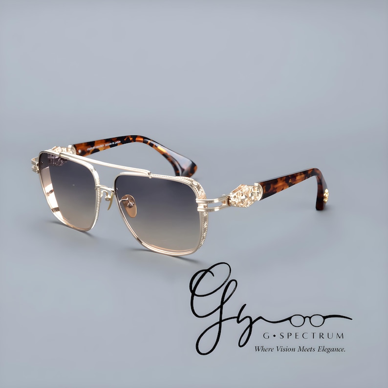 May include: Gold-coloured sunglasses with gradient lenses. The frames have a double bridge and decorative accents on the temples. The arms feature a tortoiseshell pattern. The logo "G Spectrum Where Vision Meets Elegance" is in the bottom right corner.