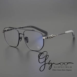 May include: Black metal eyeglasses with a double bridge and a distinctive frame shape. The temples have decorative silver accents. The lenses have a slight blue tint. The text "G Spectrum Where Vision Meets Elegance" is visible.