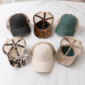 May include: Five baseball caps with mesh backs arranged in a circle. Two caps are shown from the front in black and cream, one in green. Two caps are shown from the underside, featuring leopard print and black and white floral patterns.