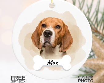 May include: A white ceramic ornament featuring a beagle dog portrait with brown and white fur. The dog's name, "Max", is written on a bone-shaped design. The ornament has a gold string for hanging. The words "CUSTOM PHOTO" are also visible.