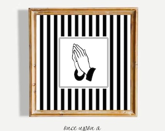 Op de afbeelding: Ingelijste kunstafdruk met een zwart-wit gestreepte achtergrond. Een witte vierkant in het midden toont een zwart-wit illustratie van biddende handen. De lijst is lichtbruin. De tekst "once upon a NICE PICTURE" staat onderaan.