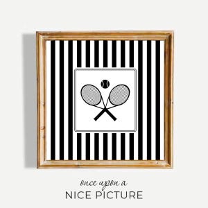 Puede incluir: Obra de arte enmarcada con temática de tenis. El fondo tiene rayas verticales en blanco y negro. Un cuadrado blanco en el centro muestra raquetas de tenis cruzadas y una pelota. El marco es de color marrón claro. El texto "once upon a NICE PICTURE" está en la parte inferior.