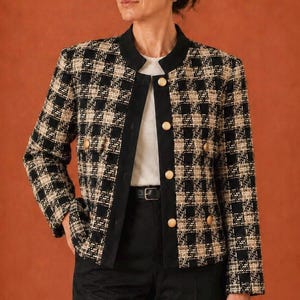 May include: A long-sleeve jacket featuring a black and beige plaid tweed pattern, a solid black mandarin collar, and a front placket with gold-toned buttons. The jacket includes two small flap pockets on the front and is worn over a white top.
