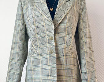 May include: A plaid blazer in shades of green, yellow, and blue, displayed on a mannequin. The blazer has a classic notched lapel, two front pockets, and a two-button closure. The garment is paired with denim shorts and a gold necklace.