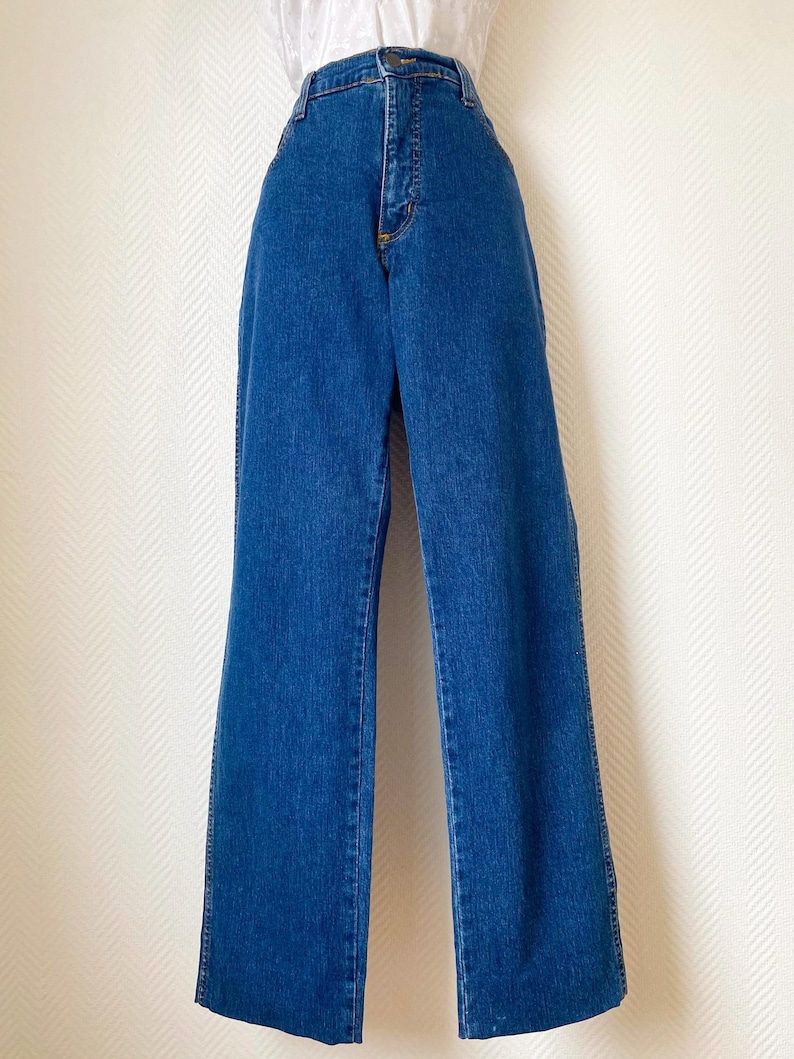 May include: Blue denim jeans with a high waist and wide leg. The jeans have a classic five-pocket design, a zipper fly, and a button closure. The denim is a medium wash, and the jeans appear to be in good condition.