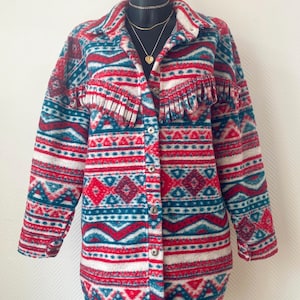 Peut inclure: Veste boutonnée à motifs sud-ouest en rouge, blanc et turquoise. La veste présente des franges sur la poitrine et un col. Elle est présentée sur un mannequin noir. Les mesures de la veste sont en centimètres.