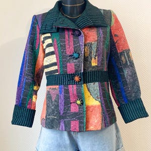 Peut inclure: Veste colorée à motifs avec un col, des poignets et une ceinture vert foncé. La veste présente un mélange de rayures verticales de différentes couleurs, dont le violet, l'orange et le bleu. Les boutons sont en forme d'étoile. La veste est associée à un short en jean.