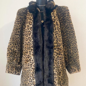 Könnte beinhalten: Ein Mantel aus Kunstfell mit Leopardenmuster in Braun- und Schwarztönen. Der Mantel hat einen schwarzen Fellbesatz an der Vorderseite und am Kragen. Das Kleidungsstück wird auf einem schwarzen Kleiderbügel präsentiert.