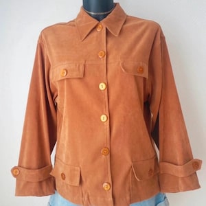 Peut inclure: Veste marron clair avec col, fermeture boutonnée et deux poches poitrine. La veste a des manches longues avec des poignets boutonnés et deux poches inférieures. La veste est présentée sur un mannequin.