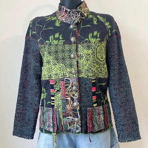 Peut inclure: Veste patchwork avec un col montant et une fermeture boutonnée. La veste présente un mélange de motifs, notamment des motifs floraux et géométriques dans des tons de vert, de noir et de rouge. Les manches sont de couleur gris foncé, de style en tricot ajouré.