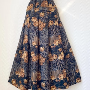 May include: A long, flowing skirt with a dark navy background and a repeating pattern of tan roses and other floral and geometric designs. The skirt has an elastic waistband and a full, A-line shape.