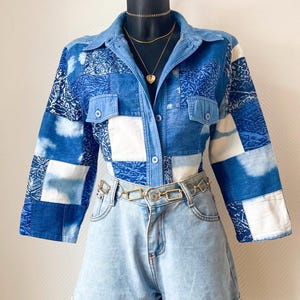 Peut inclure: Ensemble composé d'une chemise en patchwork de denim et d'un short en jean clair. La chemise présente un col, une fermeture boutonnée et deux poches poitrine. Une ceinture chaîne dorée et des colliers dorés superposés complètent le look. L'ensemble est présenté sur un mannequin noir.