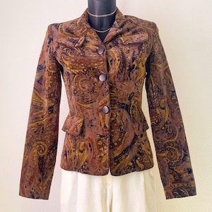 Könnte beinhalten: Ein langärmeliger Blazer mit einem Paisley-Muster in Dunkelbraun, Senfgelb und Schwarz. Die Jacke hat einen Reverskragen, drei dunkle, runde Knöpfe auf der Vorderseite sowie zwei kleine Pattentaschen auf der Brust und zwei an der Taille.