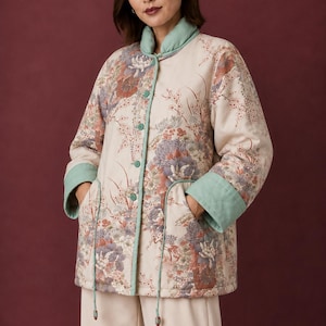 May include: A quilted jacket featuring a cream base with a multi-colored floral print in shades of purple, orange, and green. The jacket has a mandarin collar, light green trim, long sleeves with cuffs, and a front button closure with two pockets.