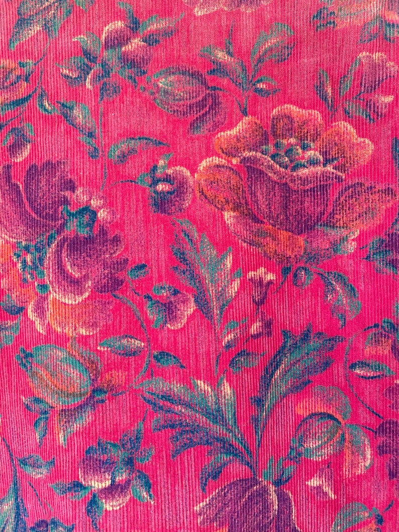 May include: A vibrant hot pink corduroy fabric featuring a repeating floral pattern. The design showcases large, blooming flowers and intricate leafy stems in shades of deep purple, dark green, and muted orange, set against the textured ribbed surface.