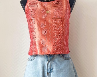 May include: A sleeveless coral-colored top featuring vertical panels of intricate raised embroidery and a round neckline, paired with light-wash blue denim shorts that have a cuffed hem and a classic five-pocket design with metal rivets.