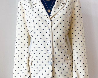May include: Cream-colored blazer with a black polka dot pattern. The blazer has a classic notched collar, button closure, and two front pockets. The garment is displayed on a black mannequin, paired with denim shorts and gold necklaces.