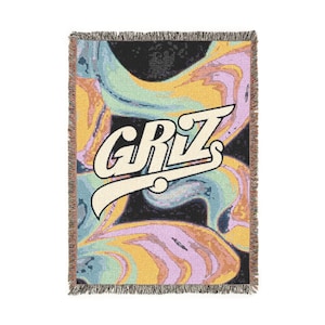 Könnte beinhalten: Eine gewebte Wurkdecke mit einem farbenfrohen, abstrakten Design mit Wirbeln aus Gelb, Blau und Lila vor einem schwarzen Hintergrund. Das Wort "GRZ" wird in einer stilisierten, cremefarbenen Schriftart angezeigt. Die Decke hat einen Fransenrand.