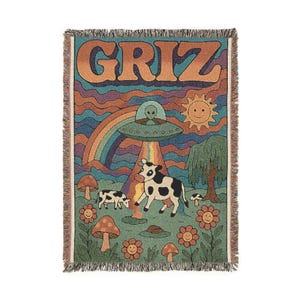 Peut inclure: Couverture tissée avec un design rétro. Elle présente le mot "GRIZ" en orange, un arc-en-ciel, un OVNI avec un extraterrestre, des vaches, des champignons et des fleurs souriantes. La palette de couleurs comprend des nuances de vert, d'orange et de violet. Bords effilochés.