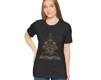 Op de afbeelding: Donkergrijs t-shirt met een goudkleurige afbeelding van een zwaard dat rozen en een open boek doorboort. Het ontwerp is gecentreerd op de voorkant. Het shirt heeft korte mouwen en een ronde hals.