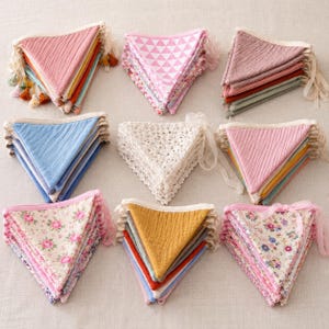 May include: A collection of colorful fabric triangle banners. The banners feature various patterns, including floral, geometric, and solid colors. Some are trimmed with lace, tassels, or ribbons. The color palette includes pinks, blues, yellows, and whites.