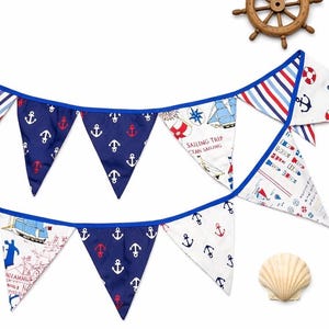 May include: Nautical-themed bunting with blue, white, and red pennants. The pennants feature anchor, sailboat, and map designs. A wooden ship's wheel and a seashell are also visible.