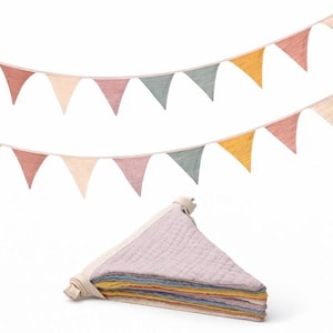 May include: A fabric bunting banner featuring two strings of triangular flags in muted shades of dusty rose, cream, sage green, and mustard yellow. Below the strings, a stack of folded triangular fabric flags in matching colors.