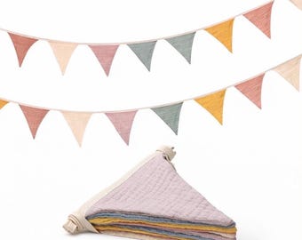 May include: A fabric bunting banner featuring two strings of triangular flags in muted shades of dusty rose, cream, sage green, and mustard yellow. Below the strings, a stack of folded triangular fabric flags in matching colors.