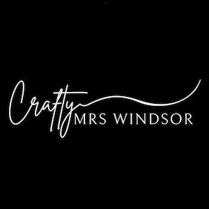 以下が含まれることがあります： 黒い背景に白いCrafty Mrs Windsorのロゴ。 「Crafty」の文字は流れるような筆記体で、「Mrs Windsor」はより標準的なフォントです。 曲がった線が単語の上にあります。