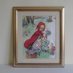 Framed book print of Little Red Riding Hood collecting flowers in the wood, present in a gold frame with a cream mount. Measures approx 35cm by 30cm by 2cm