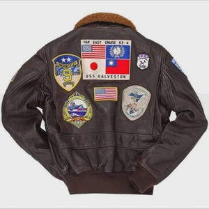 May include: A brown leather bomber jacket with a brown fur collar. The back of the jacket features several patches, including the American flag, the text "FAR EAST CRUISE 63-4", and "USS GALVESTON".