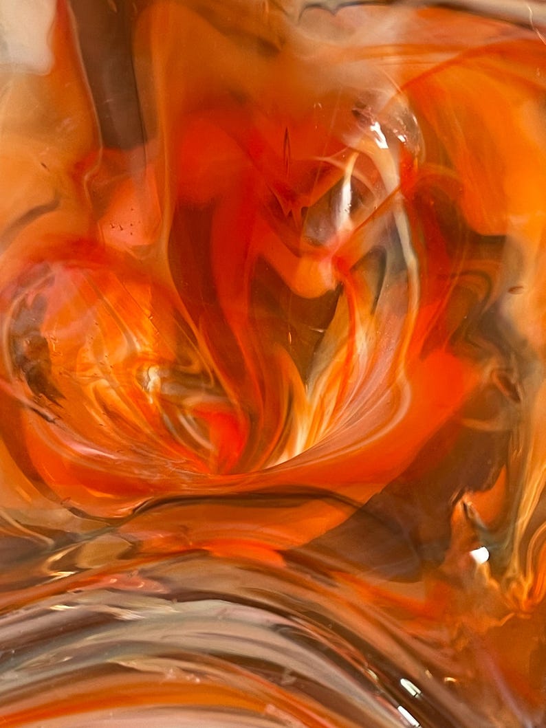 May include: Abstract artwork featuring swirling patterns of orange, red, brown, and white. The colors blend and flow, creating a dynamic and textured visual effect. The artwork evokes a sense of movement and depth.