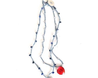 May include: A handmade necklace featuring a light blue crocheted chain adorned with blue and clear beads. The necklace has a silver bird charm and a red heart-shaped pendant. Two white buttons are at the top.