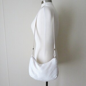 May include: White chainmail shoulder bag with a silver finish. The bag has a long strap and is worn on a white mannequin.