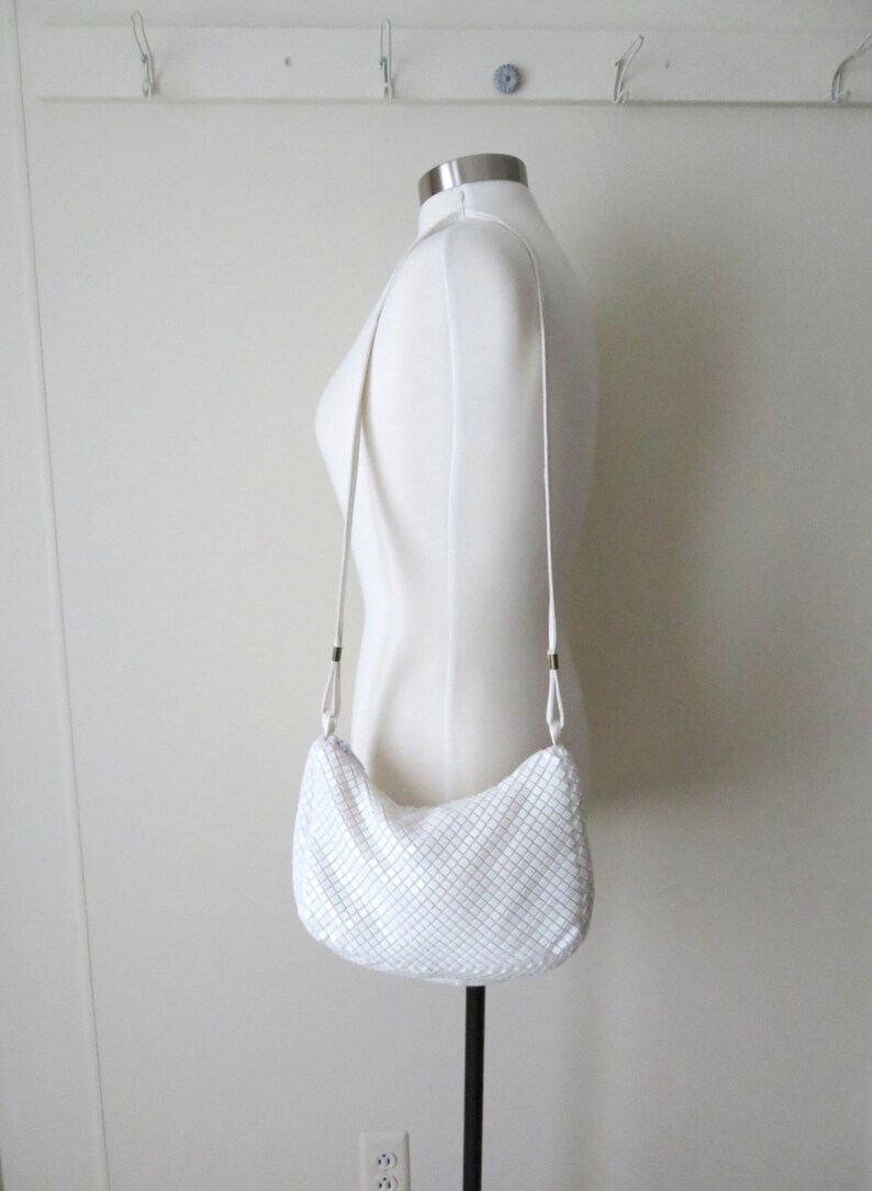 May include: White chainmail shoulder bag with a silver finish. The bag has a long strap and is worn on a white mannequin.