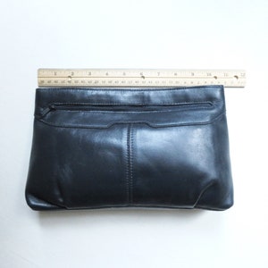May include: A black leather clutch purse with a zippered pocket and a flap closure.